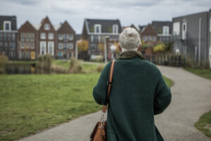 Oudere vrouw wandelt naar woningen die in de verte zichtbaar zijn
