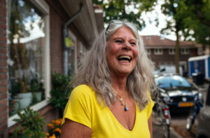 Vrouw in felgeel t-shirt staat lachend in de woonwijk