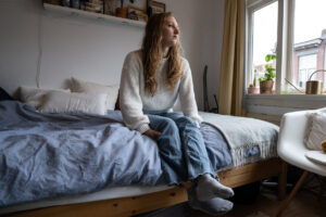 Foto bij regulering voor betaalbare woningen waarop een jonge vrouw moedeloos uit haar slaapkamerraam kijkt.